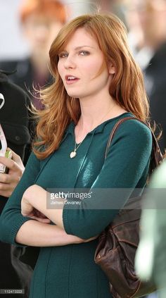 a woman with red hair is looking at her cell phone while standing in the street