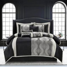 a bed with black and white comforters in front of two large arched windows,