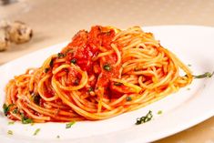 spaghetti with tomato sauce and parsley on a white plate next to some garlic bread