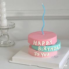 two birthday cakes sitting on top of a white table next to a candle and some candles