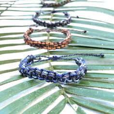 three braided bracelets sitting on top of a palm tree leaf covered in drops of water