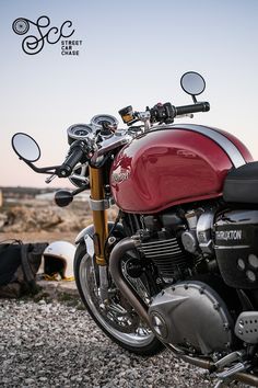 a red motorcycle parked on top of a gravel field