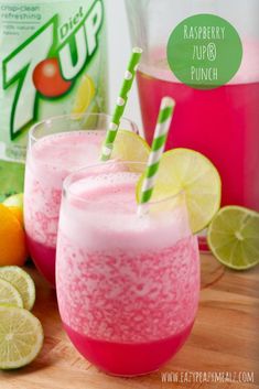 two glasses filled with pink lemonade next to sliced oranges and limes on a cutting board