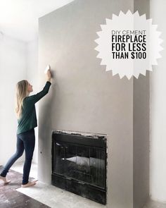 a woman is painting the wall in her living room with white paint and black fireplace