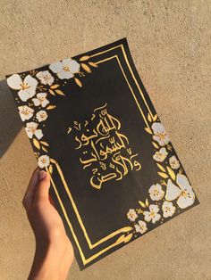 a person holding up a book with an arabic writing on it and flowers around it