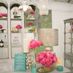 pink flowers and candles are sitting on a table in front of a white tent with chandeliers