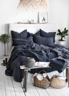 a bed with blue linens and pillows in a white room next to a plant