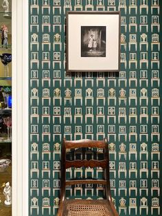 a chair sitting in front of a green wallpapered room with pictures on it