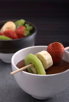 two bowls filled with fruit on top of a table next to each other and sticks sticking out of them