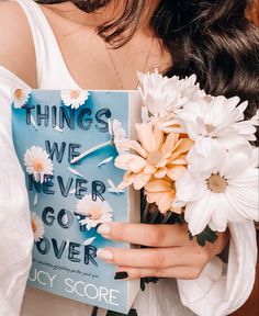 a woman holding a book with flowers in front of her and the words things we never got over written on it