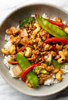 a bowl filled with rice and vegetables on top of a marble countertop next to chopsticks