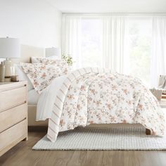 a white bed with floral comforter and pillows in a room next to a window