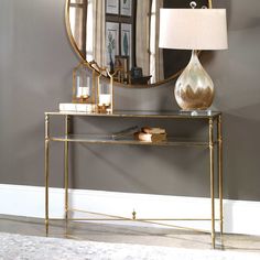 a gold console table with a lamp and mirror on the wall in front of it