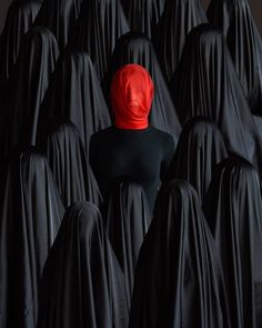 a person with a red headscarf stands among black cloaks