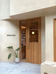 a welcome sign is on the front door of a building with a potted plant next to it