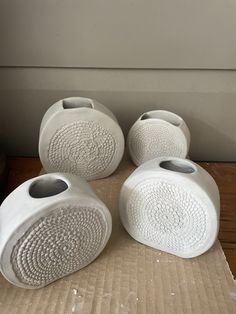 four white ceramic vases sitting on top of a cardboard box next to a window