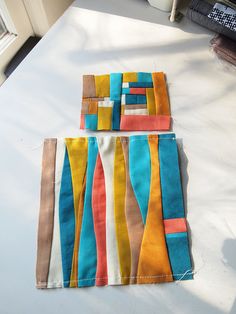 two pieces of colorful fabric sitting on top of a white table next to a window