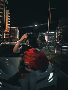 a woman sitting in the back of a white car with red flowers on it's hood