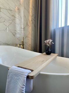 a white bath tub sitting under a window next to a vase with flowers on it