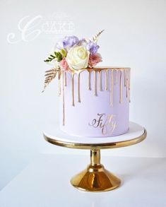 a white cake with gold drips and flowers on top is sitting on a stand