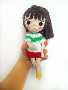 a crocheted doll is being held by a person's hand on a white background