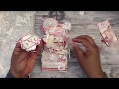 two hands are holding small pieces of paper and some other items on a wooden table