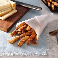 french fries are sitting in a paper wrapper on a cutting board next to other foods