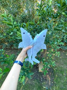 a hand holding up a blue stuffed animal that looks like a fish in the grass