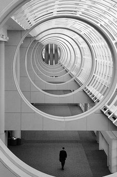 a man is walking through a large circular tunnel in the middle of an office building