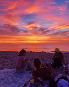 three people sitting on the beach at sunset