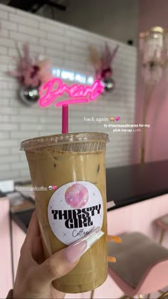 a person holding up a drink in front of a neon sign that says thirsty coffee