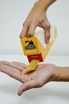 two hands are holding some kind of box with noodles on it and one hand is holding another