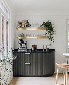 a kitchen with shelves filled with bottles and glasses next to a bar area that has plants on it