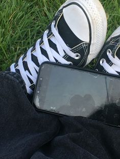 a cell phone sitting on top of a pair of black and white shoes next to someone's legs