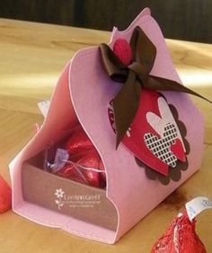 a pink box filled with lots of chocolates on top of a wooden table next to two red heart shaped candies