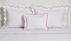 three white pillows with pink scalloped edges on a bed