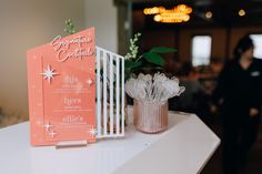 an orange and white menu sitting on top of a table next to a vase filled with flowers