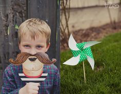 a young boy with a fake moustache on his face holding a paper pinwheel