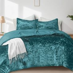 a bed covered in teal velvet with white pillows