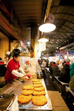 a woman cooking food on top of a metal pan in a kitchen next to other people