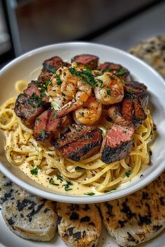 a white plate topped with pasta covered in meat and shrimp next to garlic crackers