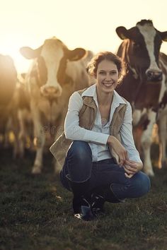 a woman kneeling down in front of cows on a field with the sun behind her