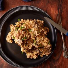 a black plate topped with rice and meat next to a fork on top of a wooden table