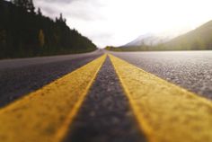 an empty road with yellow lines on the side and mountains in the background at sunset