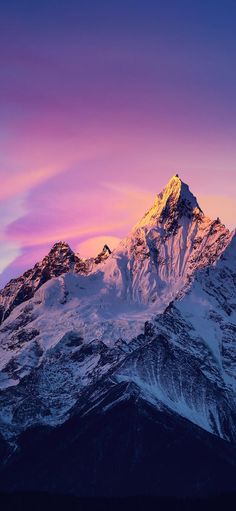 the top of a snow covered mountain with pink and purple clouds in the sky above it