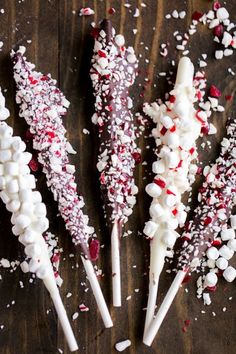 four marshmallow and pepper cane sticks on a wooden table with sprinkles