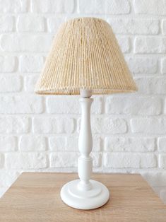 a white table lamp sitting on top of a wooden table next to a brick wall