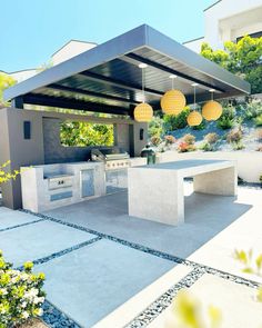 an outdoor kitchen and grill area with lights hanging from the ceiling over it, surrounded by greenery