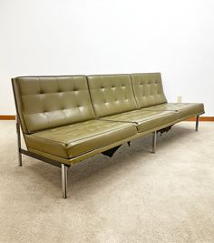 a green leather couch sitting on top of a carpeted floor next to a white wall