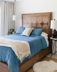 a bed with blue sheets and pillows in a bedroom next to a lamp on a table